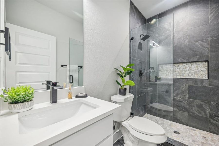 Bathroom featuring toilet, a tile shower, and vanity