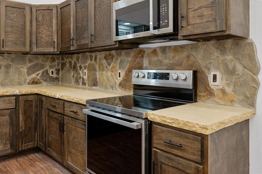 Kitchen with dark brown cabinetry, stainless steel appliances, dark hardwood / wood-style floors, and tasteful backsplash