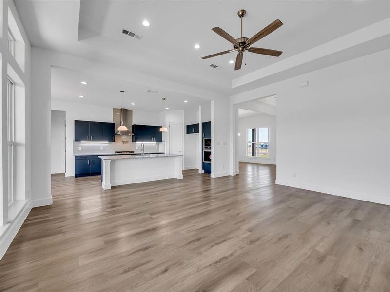 Unfurnished living room featuring sink, ceiling fan, a raised ceiling, and light hardwood / wood-style flooring