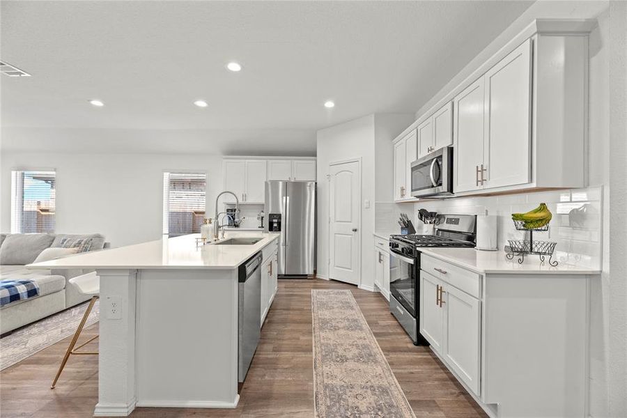 Kitchen features include quartz countertops paired with a coordinating backsplash, stainless steel appliances, crisp white cabinets with updated hardware, recessed lighting, and a sprawling island with breakfast bar seating.