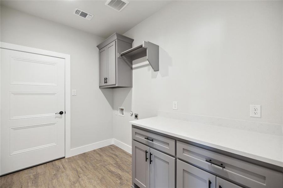 Clothes washing area featuring hookup for a washing machine, hookup for an electric dryer, light hardwood / wood-style flooring, and cabinets