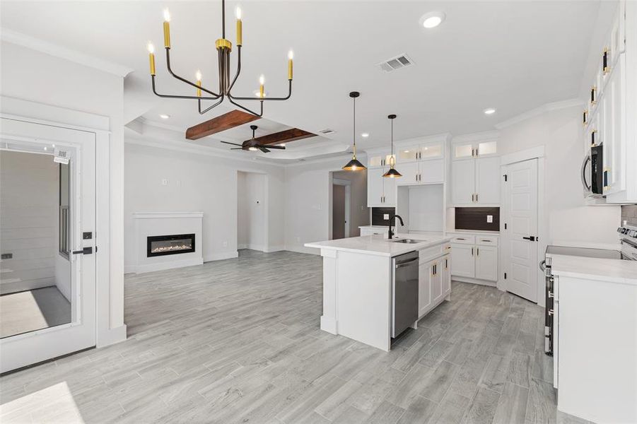 Kitchen with decorative light fixtures, ceiling fan with notable chandelier, stainless steel appliances, light hardwood / wood-style floors, and an island with sink