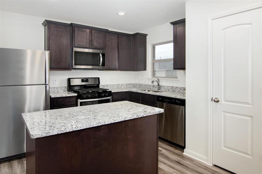 Kitchen with light wood-type flooring, stainless steel appliances, a center island, sink, and dark brown cabinetry