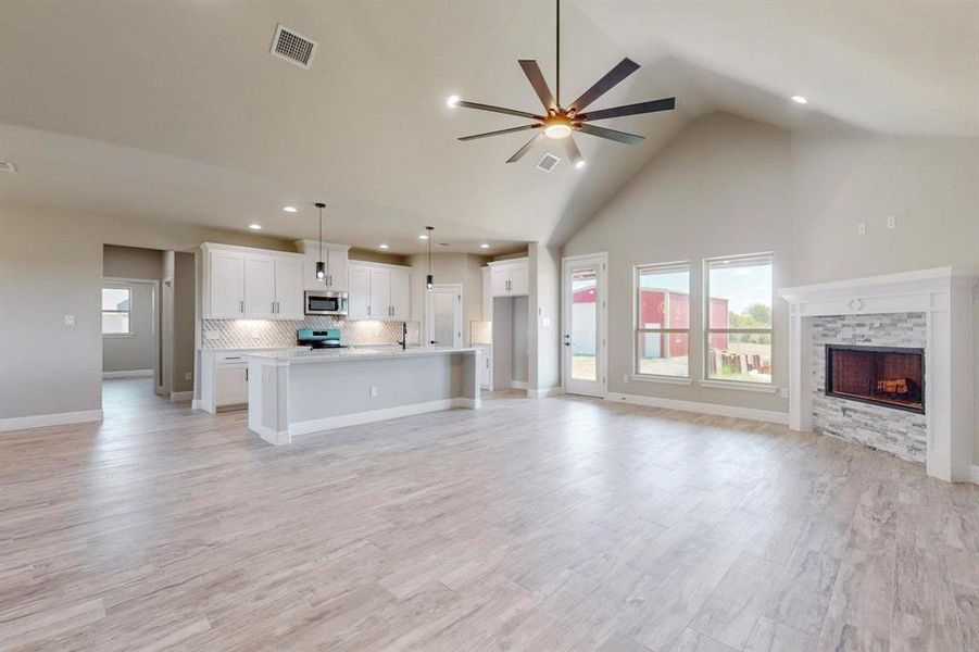 Unfurnished living room with light hardwood / wood-style floors, sink, high vaulted ceiling, a stone fireplace, and ceiling fan