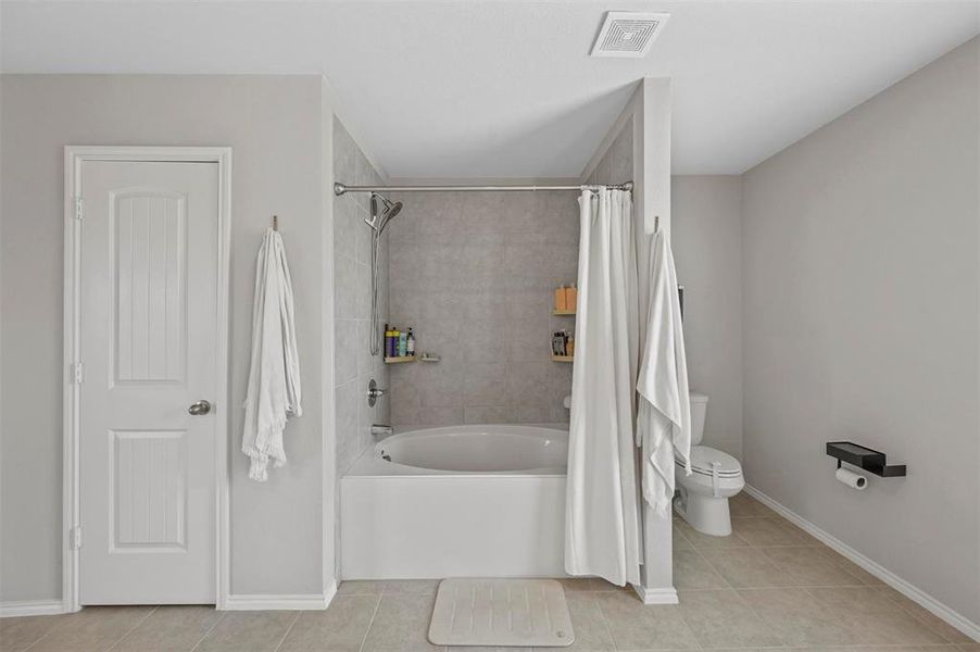 Bathroom featuring shower / bathtub combination with curtain, tile patterned flooring, and toilet