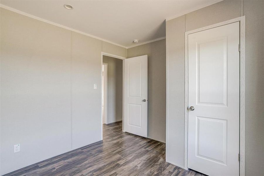 Unfurnished bedroom featuring crown molding and dark wood-type flooring