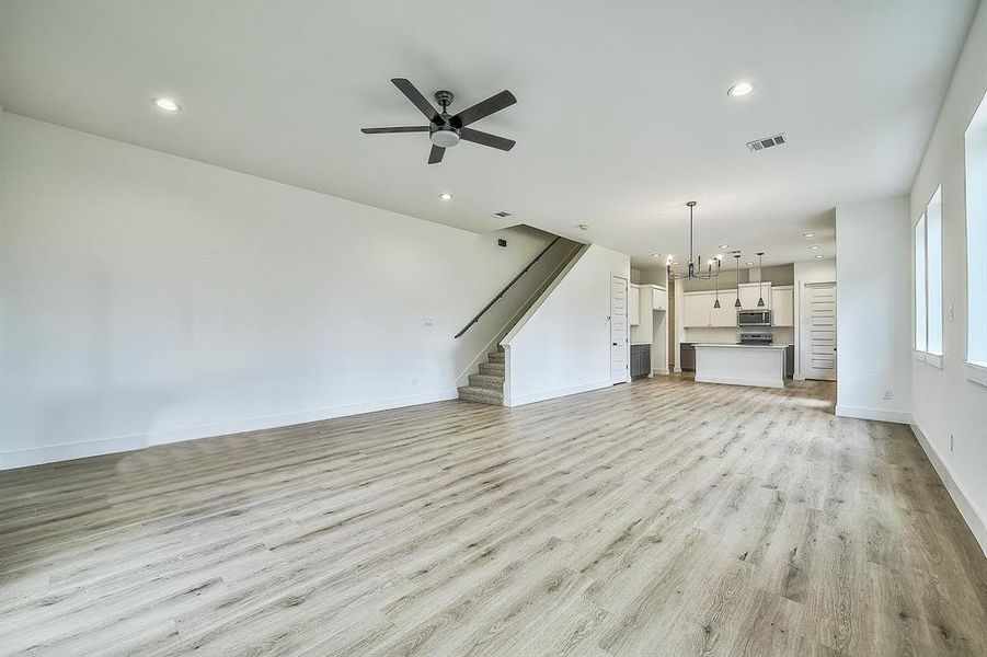 Unfurnished living room featuring light wood-type flooring and ceiling fan with notable chandelier