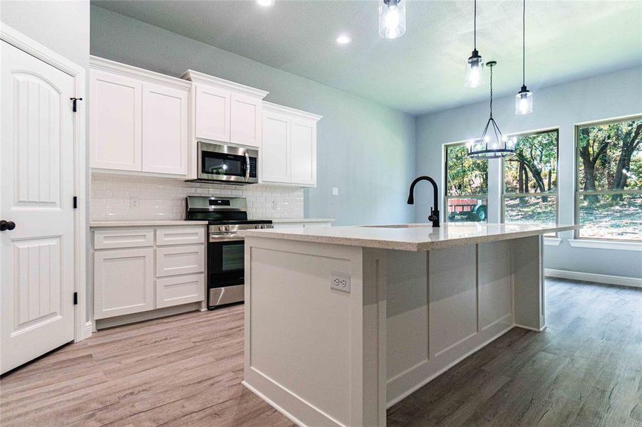 Kitchen featuring stainless steel appliances, white cabinets, hardwood / wood-style flooring, and decorative light fixtures
