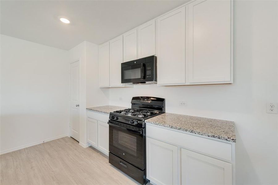 Kitchen featuring black appliances, white cabinetry, light stone counters, and light wood-type flooring