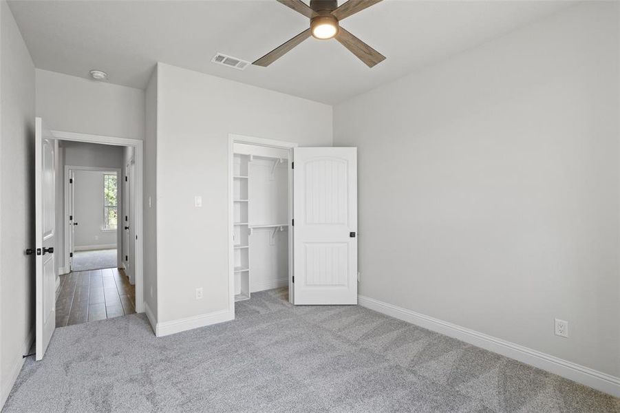 Unfurnished bedroom with a walk in closet, carpet flooring, a closet, and ceiling fan