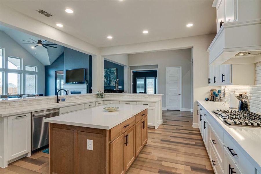 Kitchen with hardwood floors, kitchen peninsula, tasteful backsplash, stainless appliances and white cabinetry.