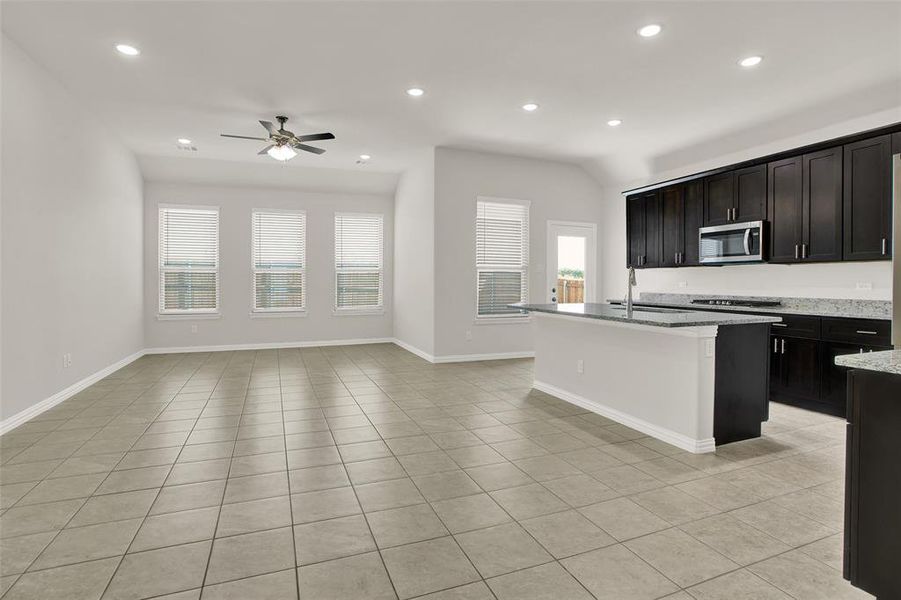 Kitchen featuring an island with sink, light stone countertops, ceiling fan, and light tile floors