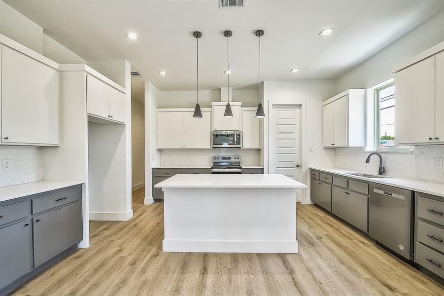 Kitchen with white cabinets, a center island, decorative light fixtures, appliances with stainless steel finishes, and sink