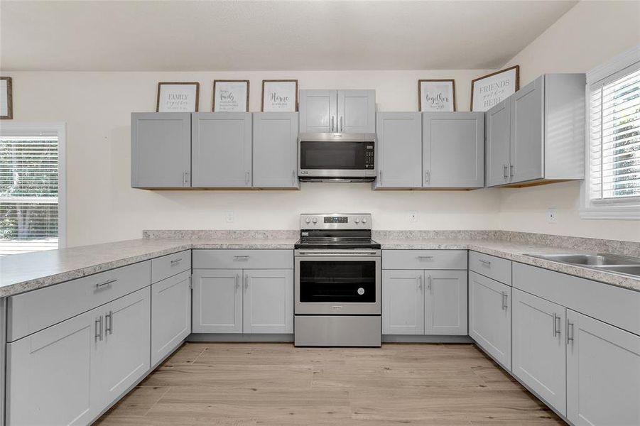 This photo showcases a modern kitchen cabinets, stainless steel appliances, formica countertops, and light tile flooring. Bright and welcoming with ample storage space.