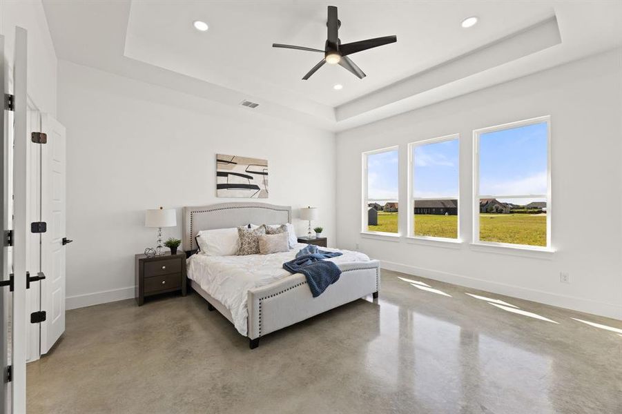 Bedroom with multiple windows, a tray ceiling, concrete floors, and ceiling fan