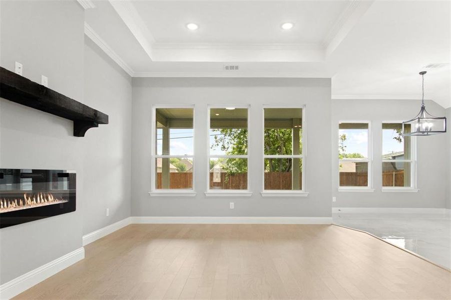 Unfurnished living room with light wood-type flooring, a raised ceiling, a chandelier, and ornamental molding