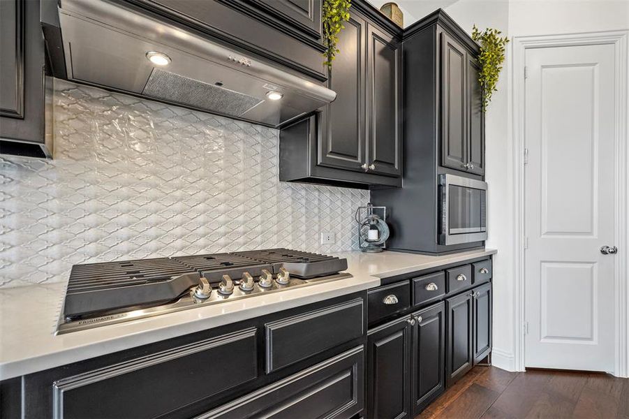 Kitchen featuring cooktop, premium range hood, backsplash, and dark wood-type flooring