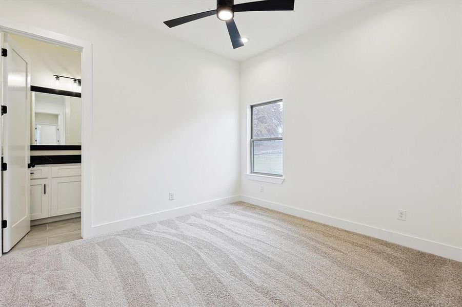 Unfurnished bedroom featuring light carpet, ensuite bath, and ceiling fan