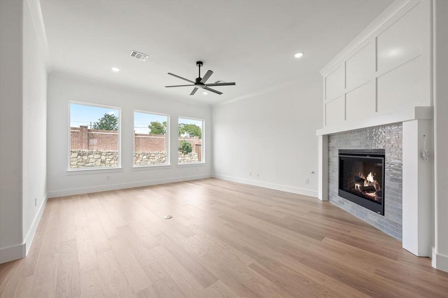 Unfurnished living room with ornamental molding, a fireplace, ceiling fan, and light wood-type flooring