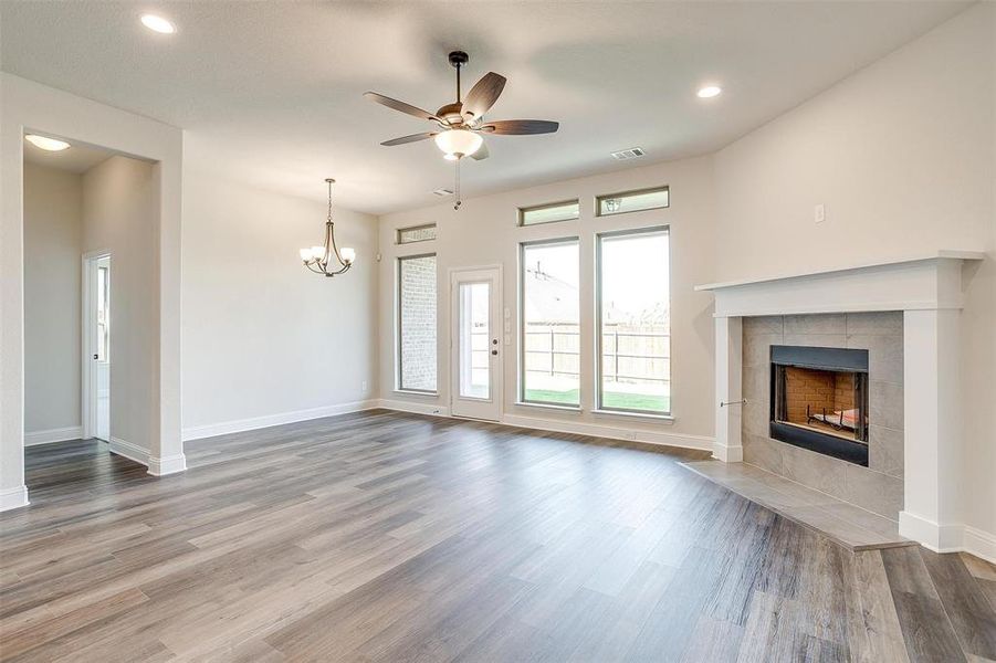 Unfurnished living room with ceiling fan with notable chandelier, a tiled fireplace, and hardwood / wood-style flooring