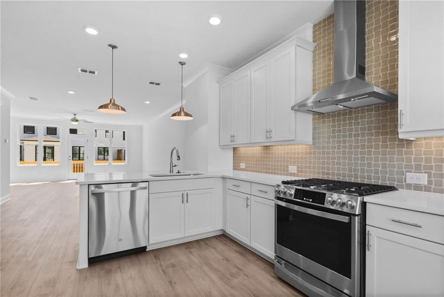 Kitchen with white cabinets, sink, wall chimney exhaust hood, stainless steel appliances, and light hardwood / wood-style floors