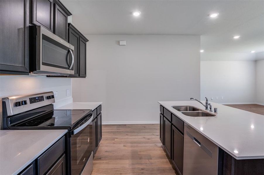 Kitchen featuring an island with sink, appliances with stainless steel finishes, light hardwood / wood-style flooring, dark brown cabinetry, and sink