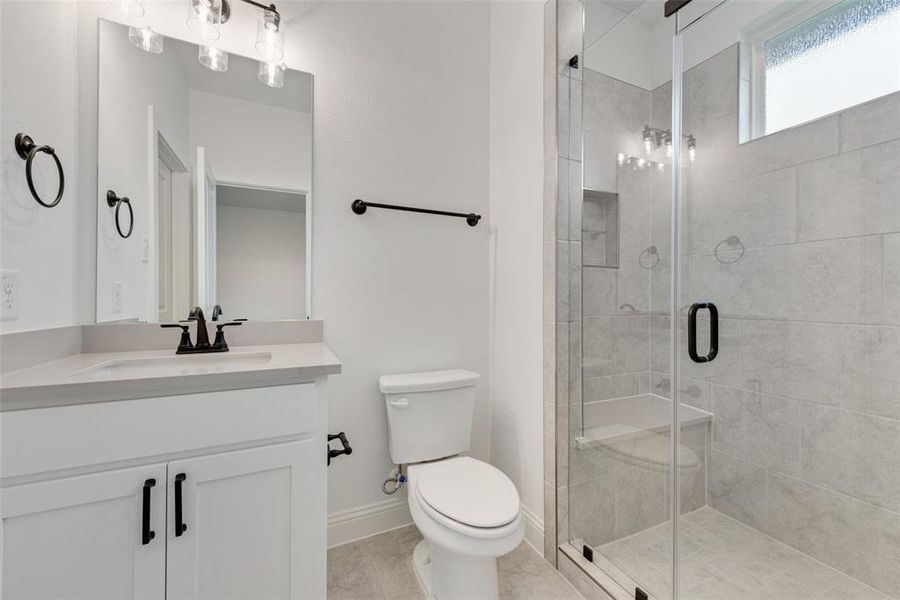 Bathroom featuring a shower with shower door, tile patterned flooring, toilet, and vanity