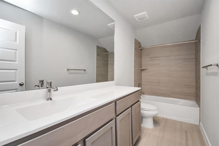 Secondary bath features tile flooring, bath/shower combo with tile surround, slate stained wood cabinets, beautiful light countertop. Sample photo of completed home with similar floor plan. Actual colors and selections may vary.