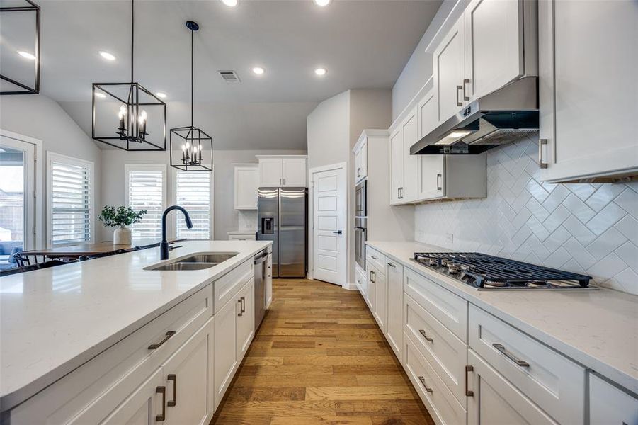 Kitchen featuring an island, lantern pendant lighting, stainless steel appliances, and white cabinetry