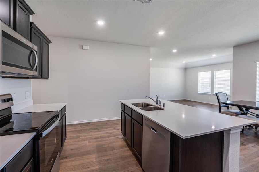 Kitchen featuring appliances with stainless steel finishes, sink, an island with sink, dark brown cabinetry, and dark wood-type flooring