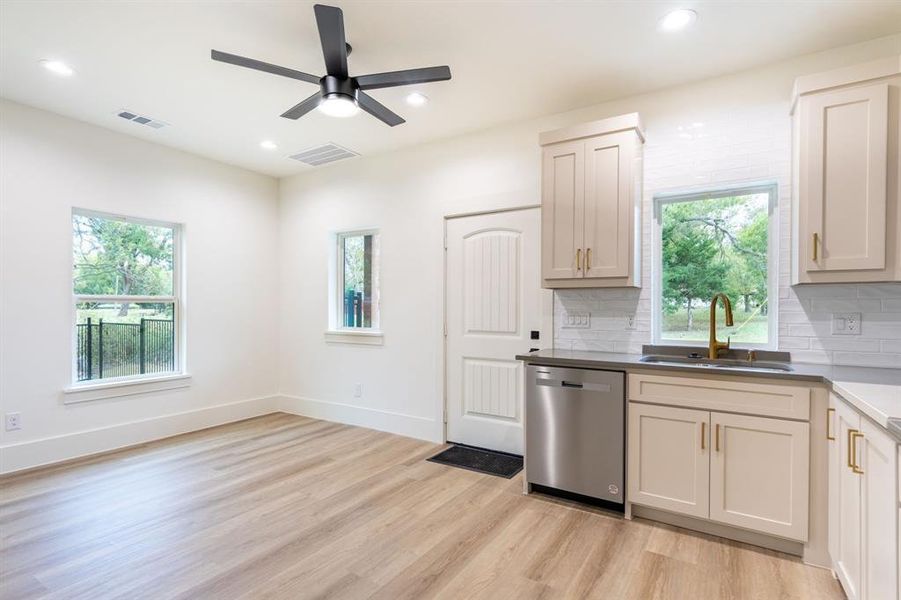 Kitchen featuring sink, stainless steel dishwasher, ceiling fan, backsplash, and light hardwood / wood-style flooring