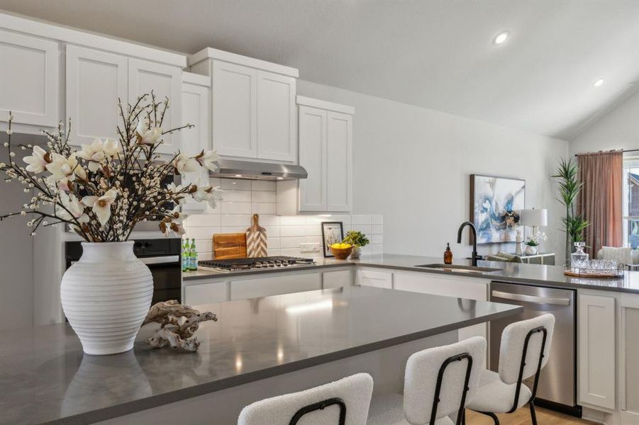 Kitchen with stainless steel appliances, white cabinetry, extractor fan, sink, and vaulted ceiling