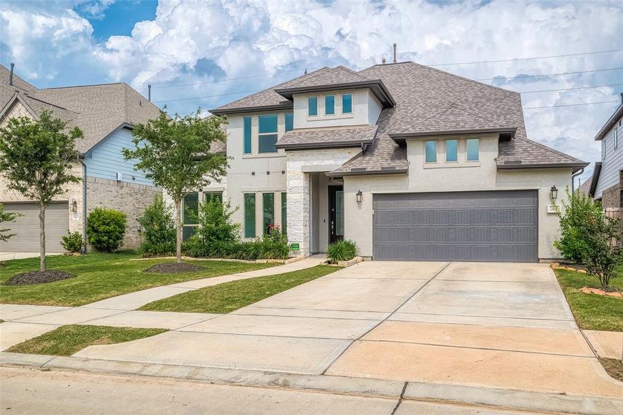 Modern two-story home with a clean design featuring a two-car garage, neatly landscaped yard, and a welcoming entrance.