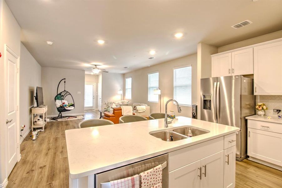 Kitchen featuring light wood-type flooring, a center island with sink, white cabinets, sink, and ceiling fan