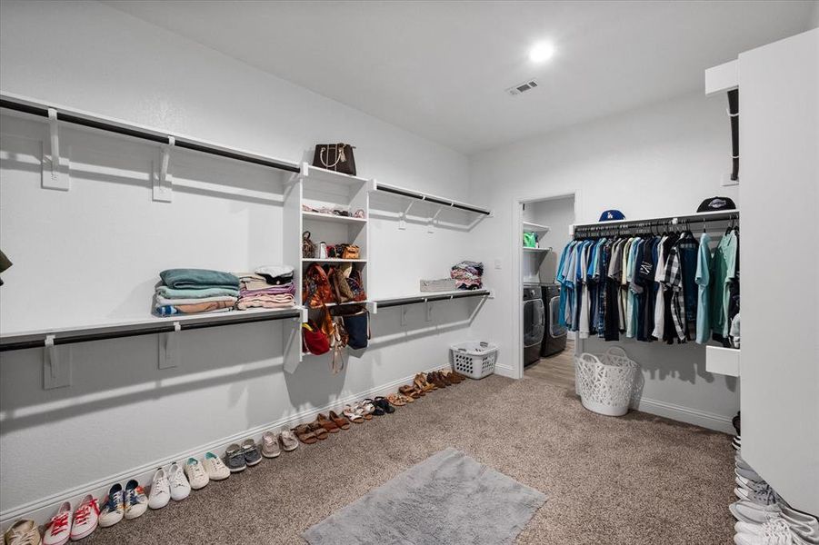 Primary bedroom spacious closet with carpet, door connection to washer and clothes dryer