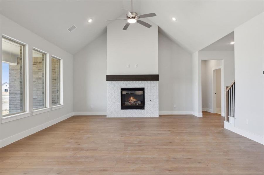Unfurnished living room with ceiling fan, light hardwood / wood-style floors, a tiled fireplace, and high vaulted ceiling