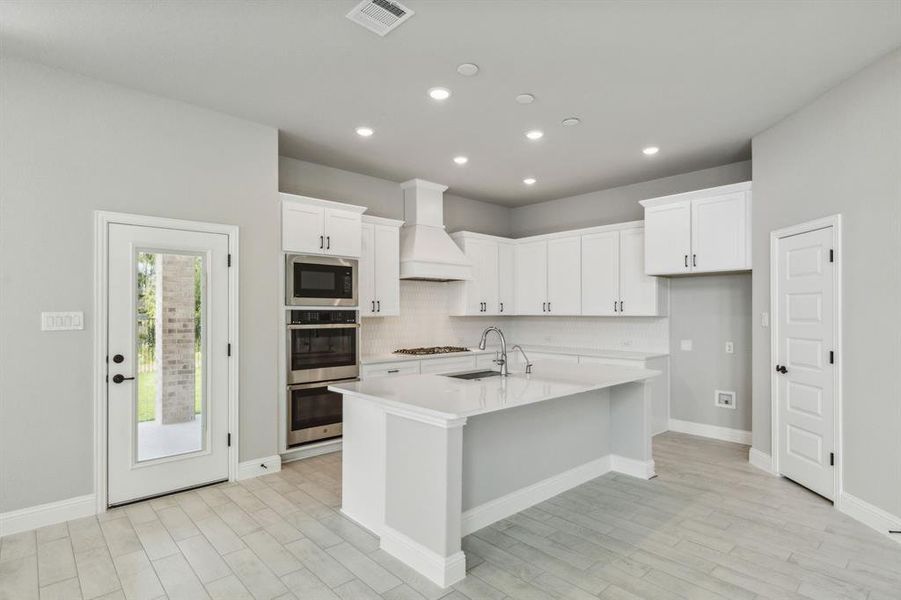 Kitchen with custom range hood, white cabinetry, sink, and a kitchen island with sink