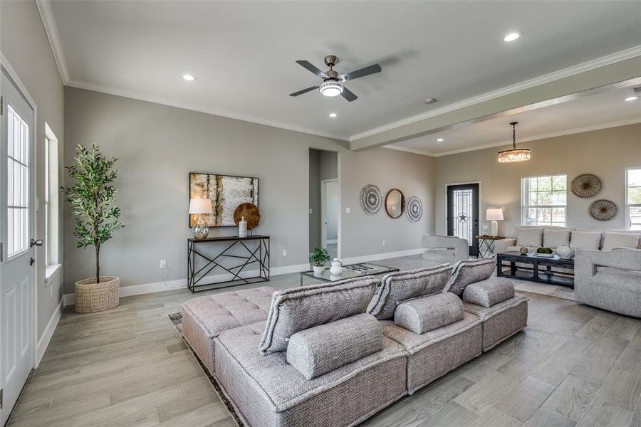 Family room featuring ceiling fan with notable chandelier, ornamental molding, and light wood-type flooring