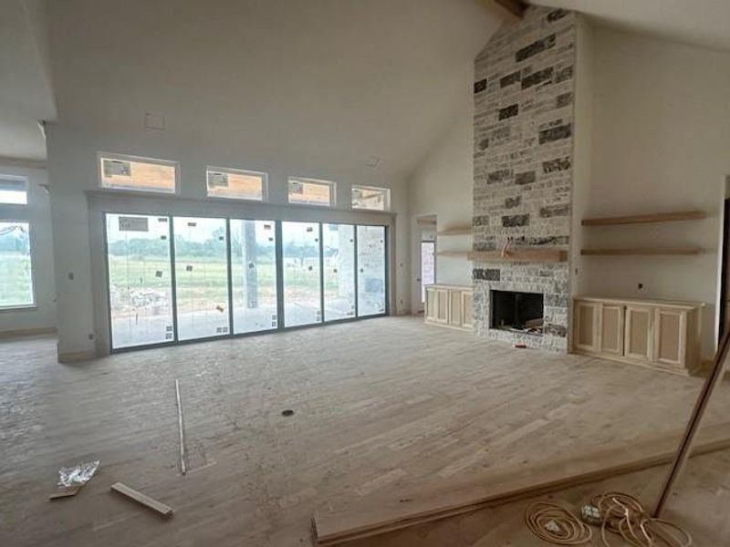 Unfurnished living room with high vaulted ceiling and a stone fireplace