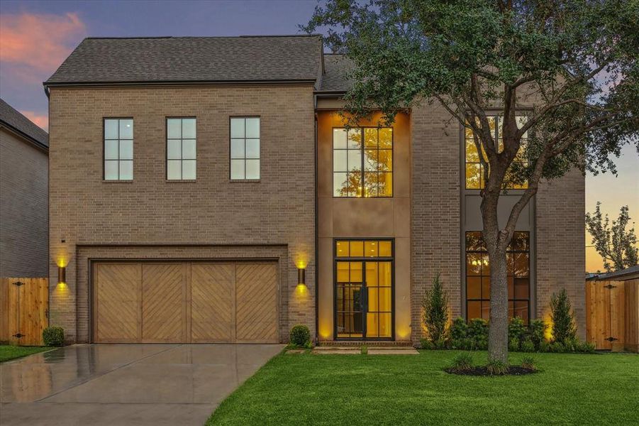 Stunning two-story modern home featuring a brick façade with large picture windows, elegant wood accents, and contemporary outdoor lighting. A spacious oversized two-car garage completes the clean and sophisticated curb appeal.