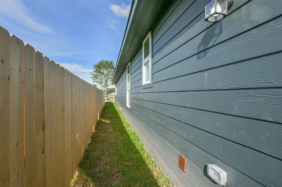 This photo shows the side of a blue house with a privacy fence along the property line, providing a secure and private outdoor space.