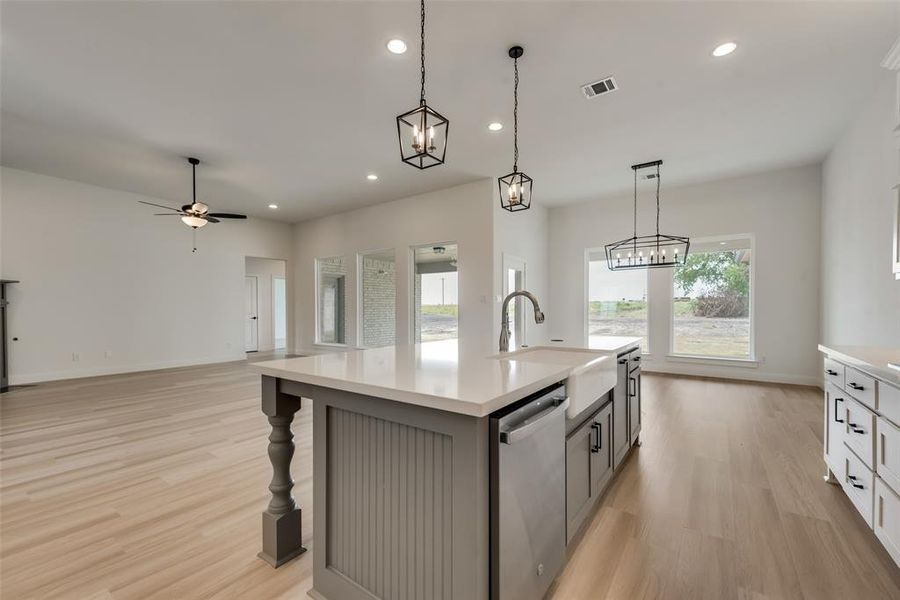 Kitchen featuring hanging light fixtures, a center island with sink, stainless steel dishwasher, and light hardwood / wood-style flooring
