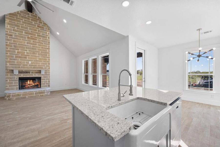 Kitchen with dishwashing machine, light wood-type flooring, light stone countertops, brick wall, and a center island with sink