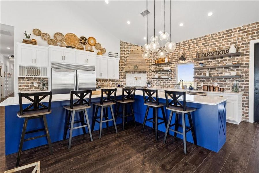 Kitchen featuring white cabinetry, a breakfast bar, a spacious island, and stainless steel built in refrigerator