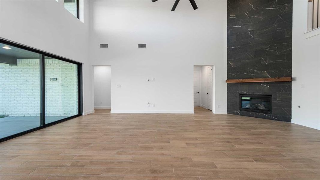 Unfurnished living room featuring light hardwood / wood-style flooring, a stone fireplace, a high ceiling, and ceiling fan