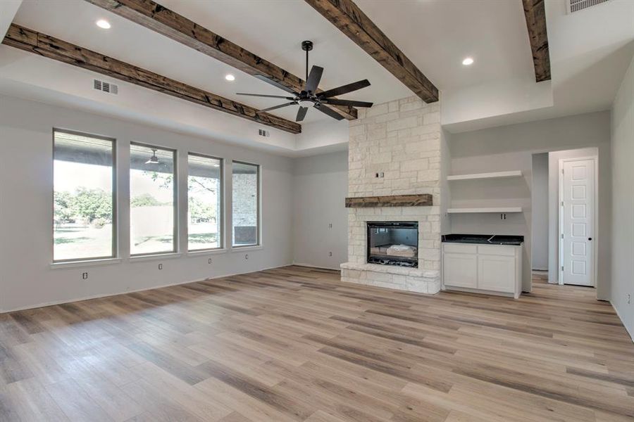 Unfurnished living room featuring light hardwood / wood-style floors, a stone fireplace, beamed ceiling, and ceiling fan