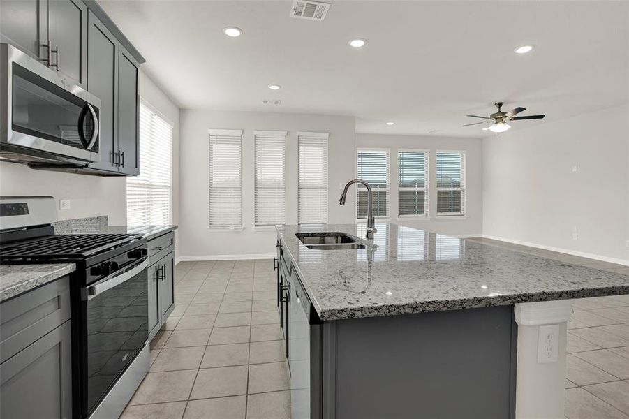 Kitchen featuring stainless steel appliances, a center island with sink, ceiling fan, sink, and light tile floors