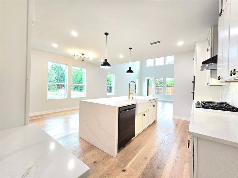 Kitchen featuring white cabinetry, an island with sink, black dishwasher, light hardwood / wood-style floors, and gas stovetop