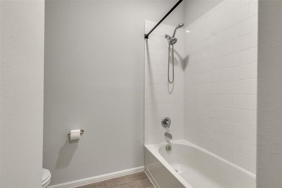 Bathroom with tiled shower / bath combo, hardwood / wood-style floors, and toilet