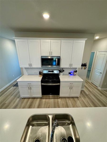 Kitchen with stainless steel appliances, sink, white cabinetry, and light hardwood / wood-style flooring